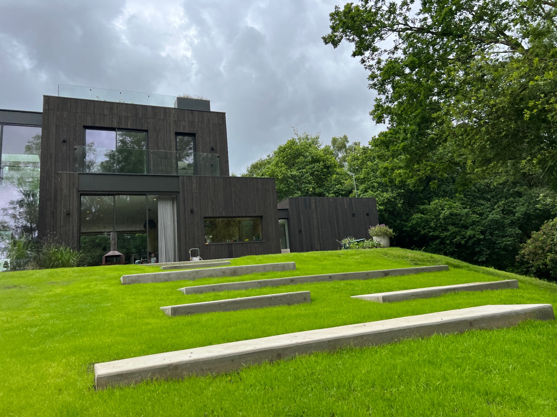 Cantilevered concrete steps rising through the lawn toward the timber-clad home