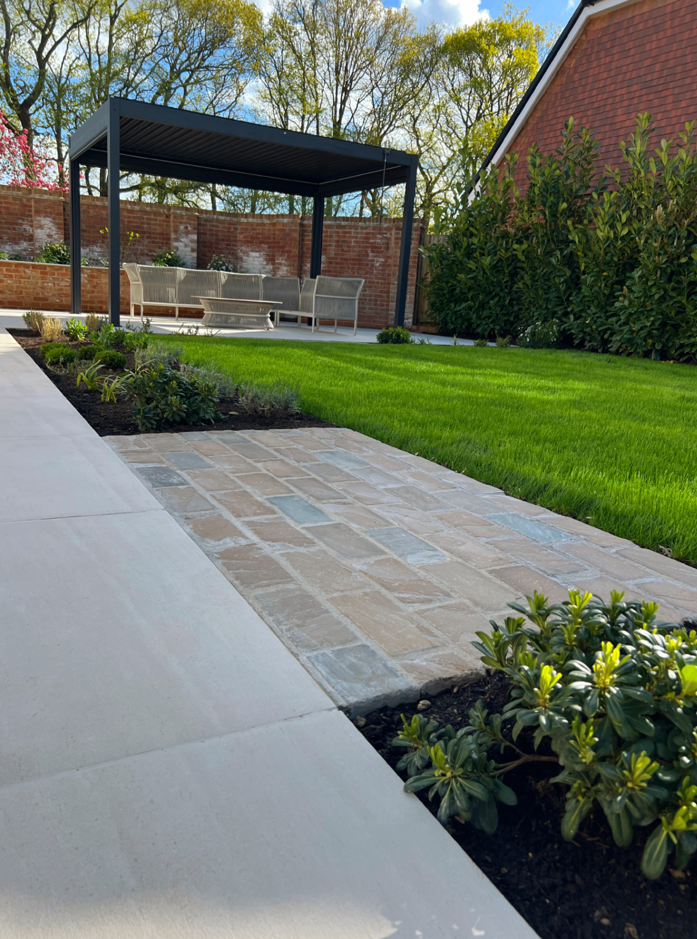 Pergola viewed across the lawn with sandstone path and planting borders