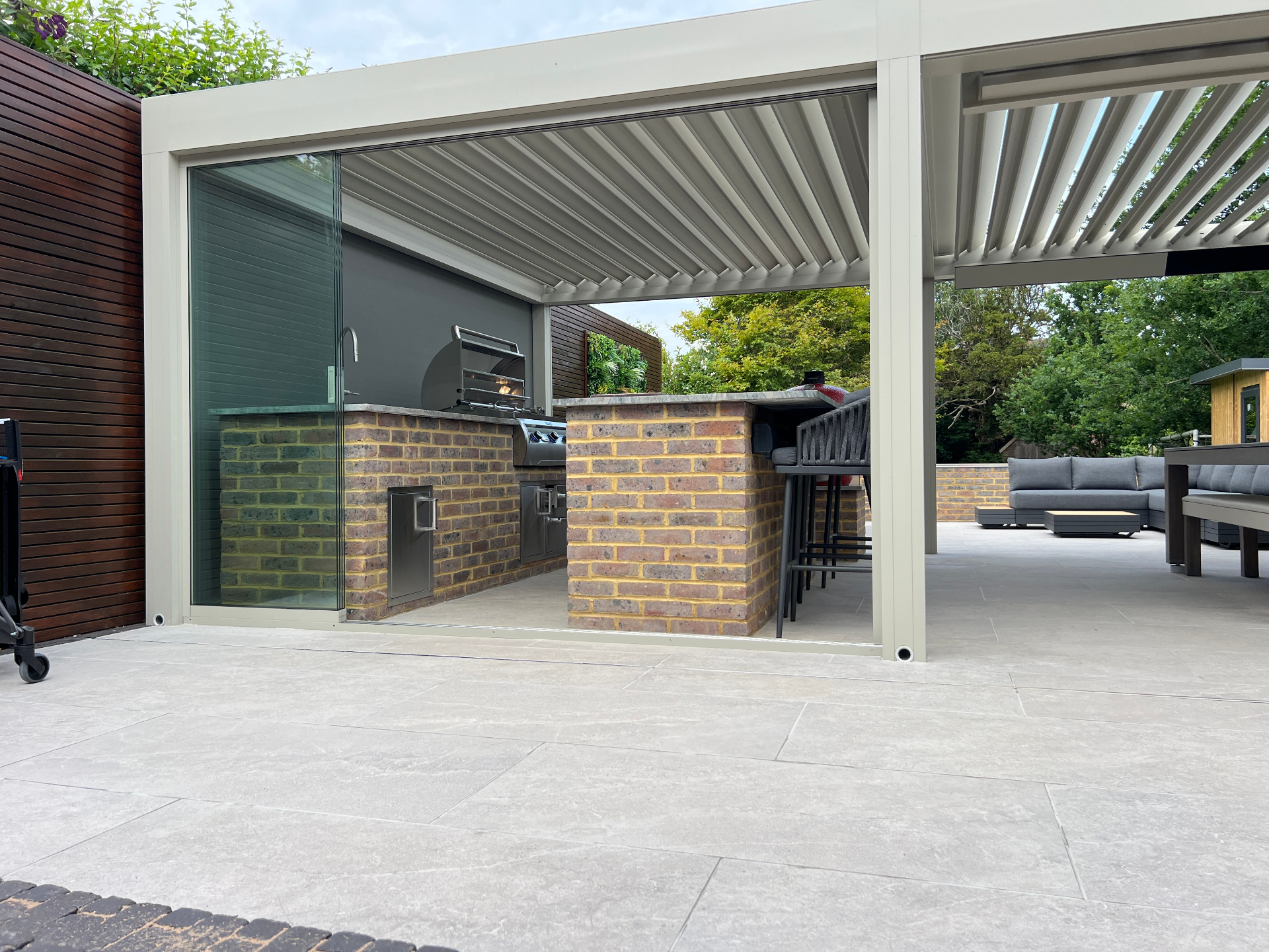 Louvered pergola covering outdoor kitchen and pool table area