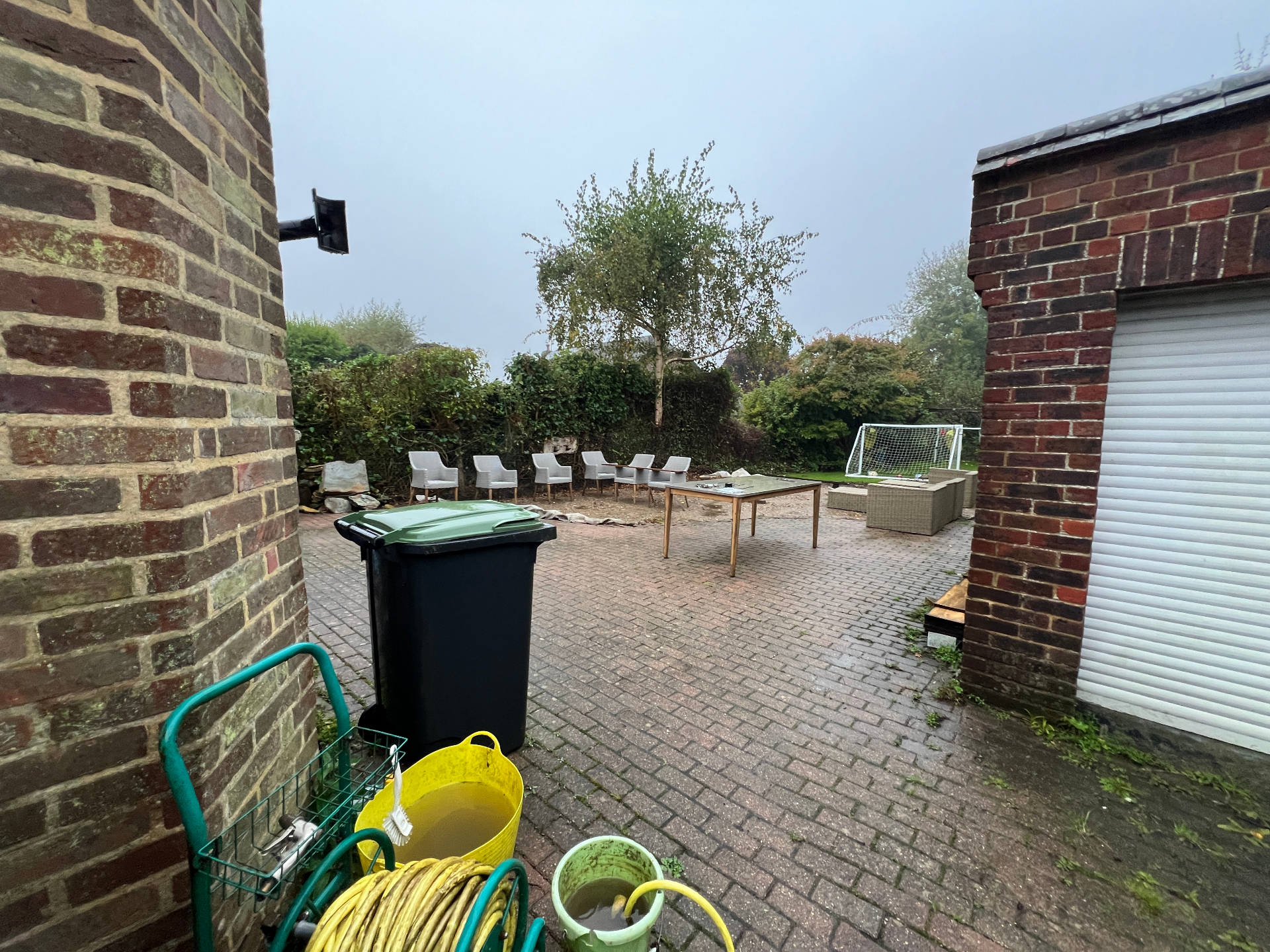 Original family garden — worn block paving with mismatched furniture against brick walls