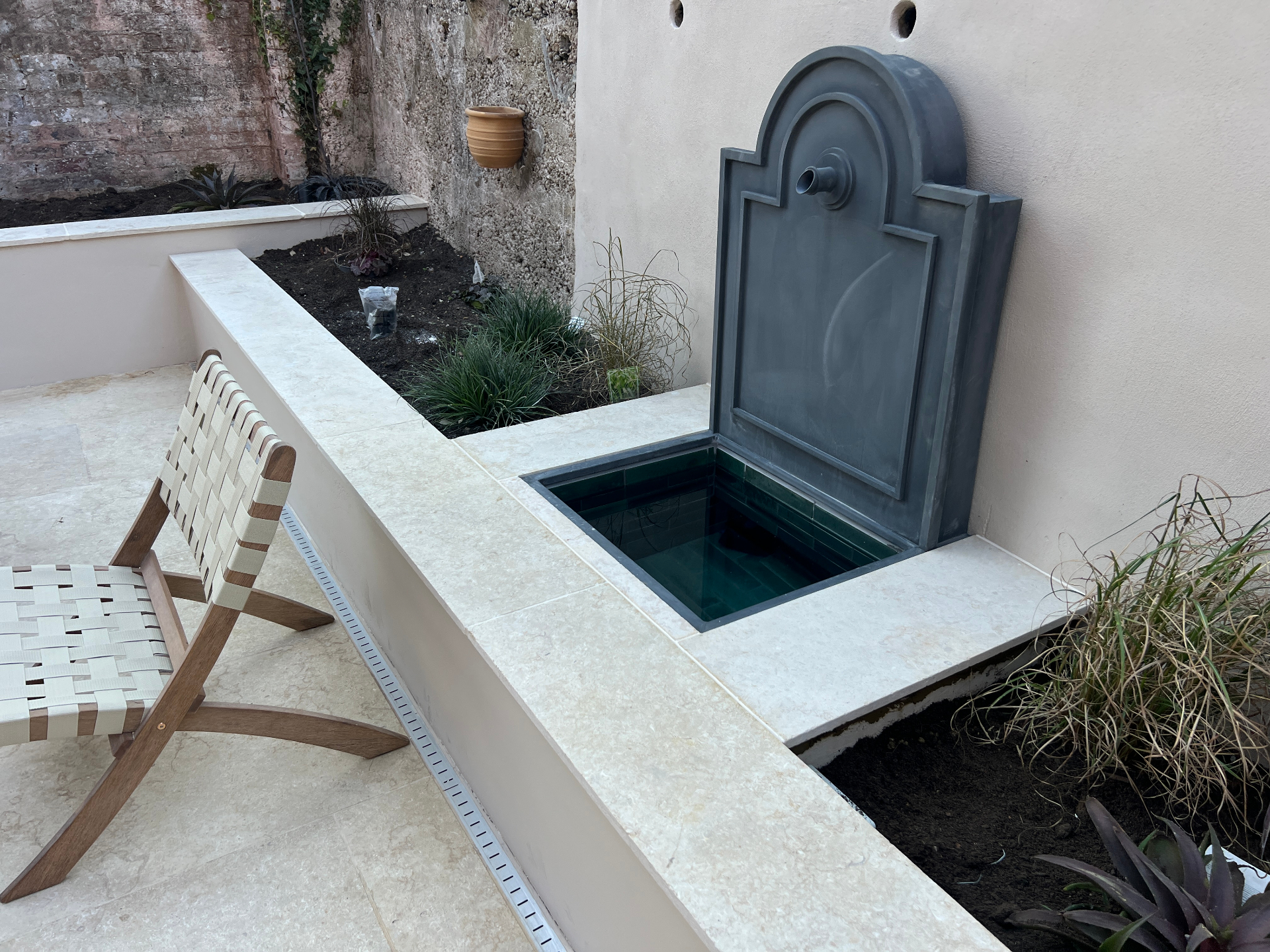 Medi Garden — lead wall fountain with green-tiled basin set into a travertine-capped raised bed