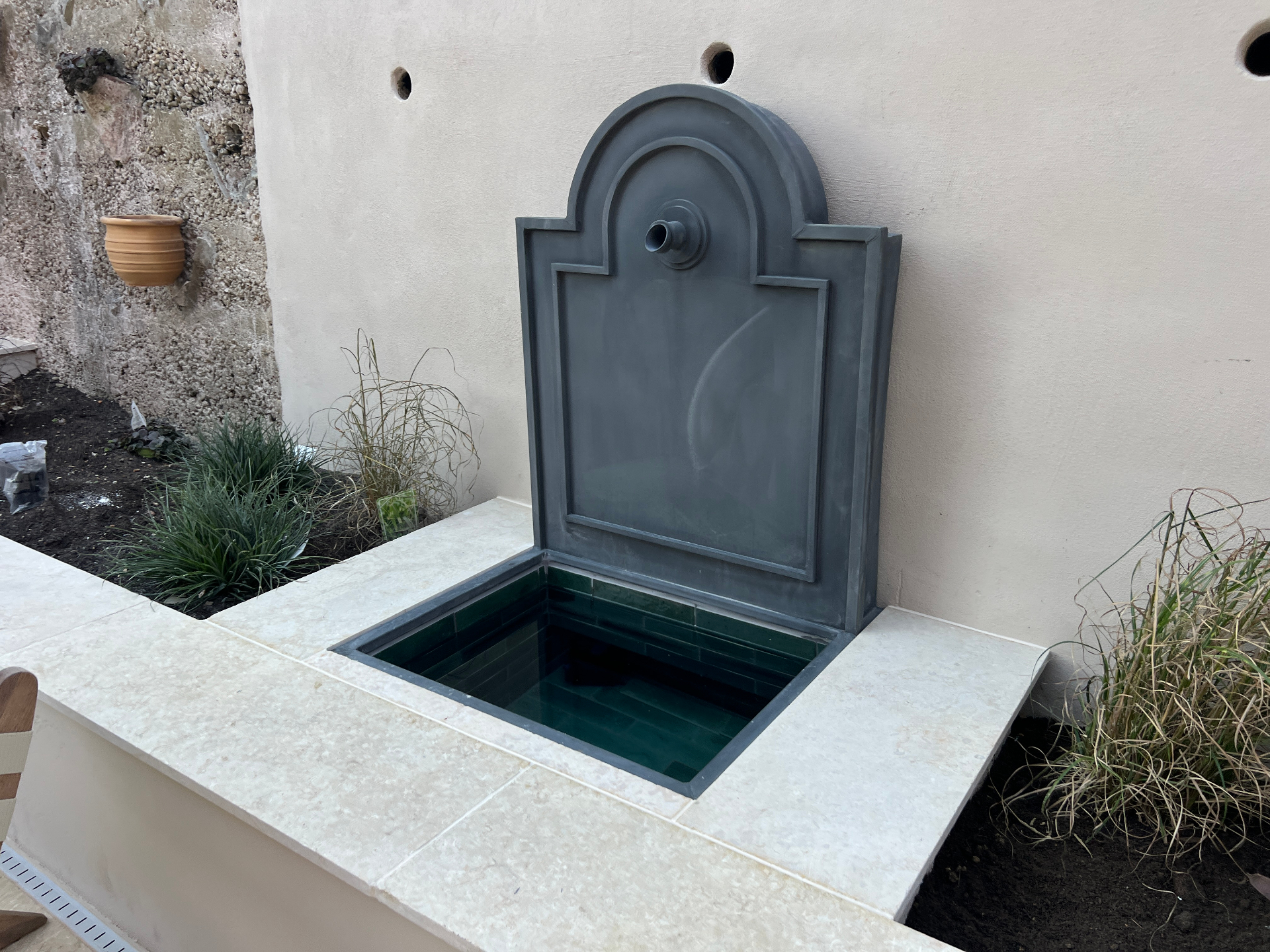 Medi Garden — lead fountain against the lime-rendered wall with grasses and terracotta pot
