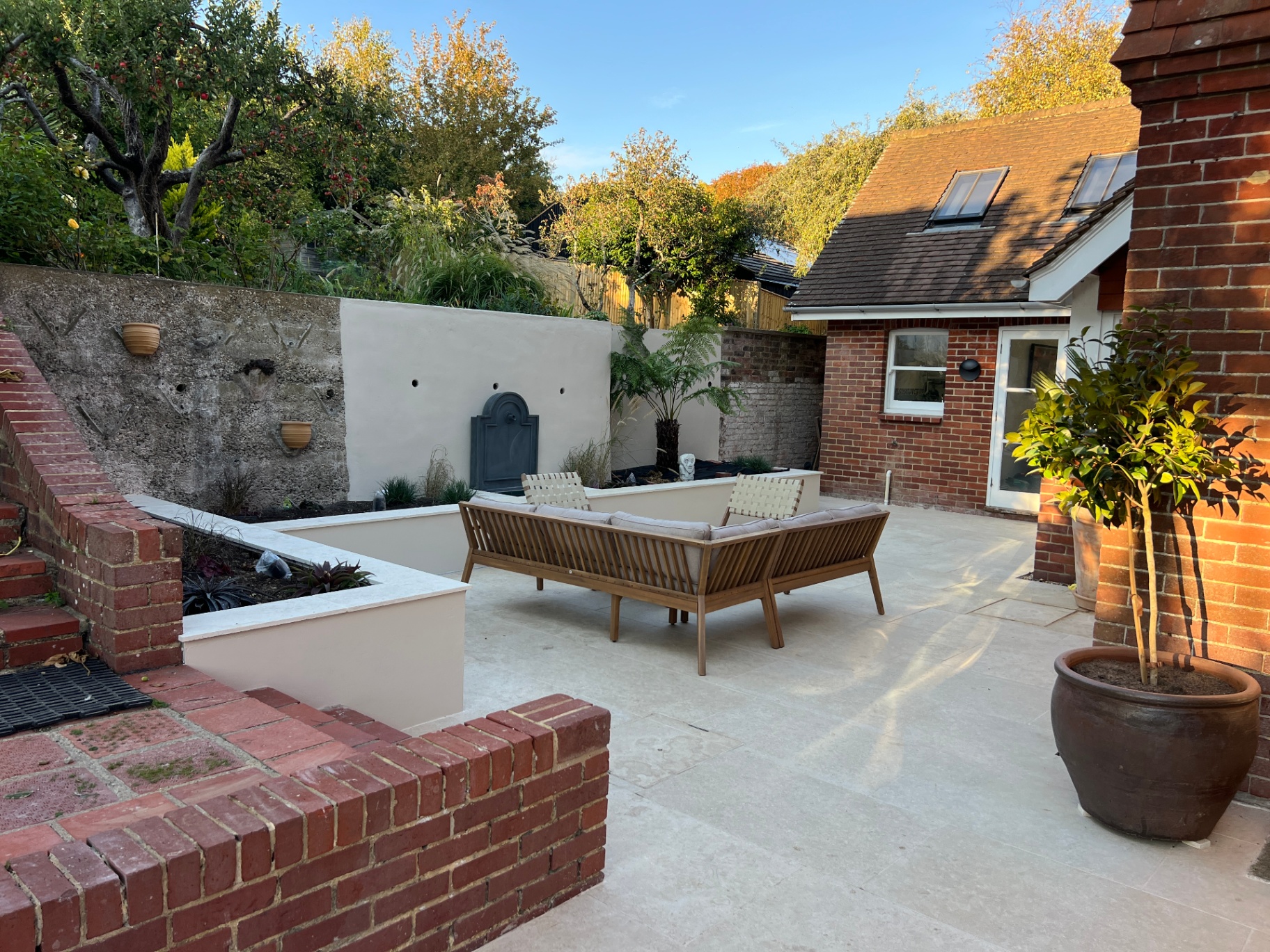 Medi Garden — full courtyard view with rendered wall, raised beds and timber sofa on travertine paving