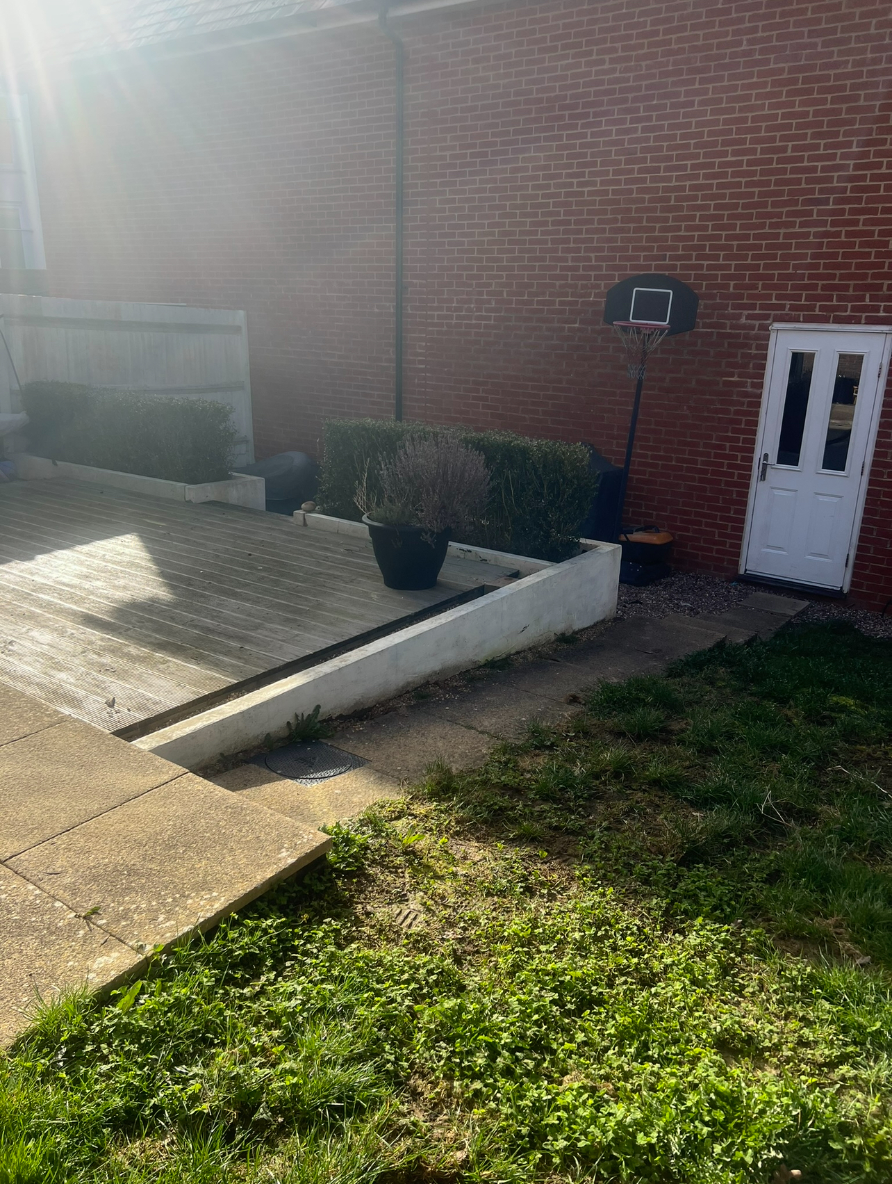 Original garden — tired timber decking and rendered retaining wall beside a patchy lawn