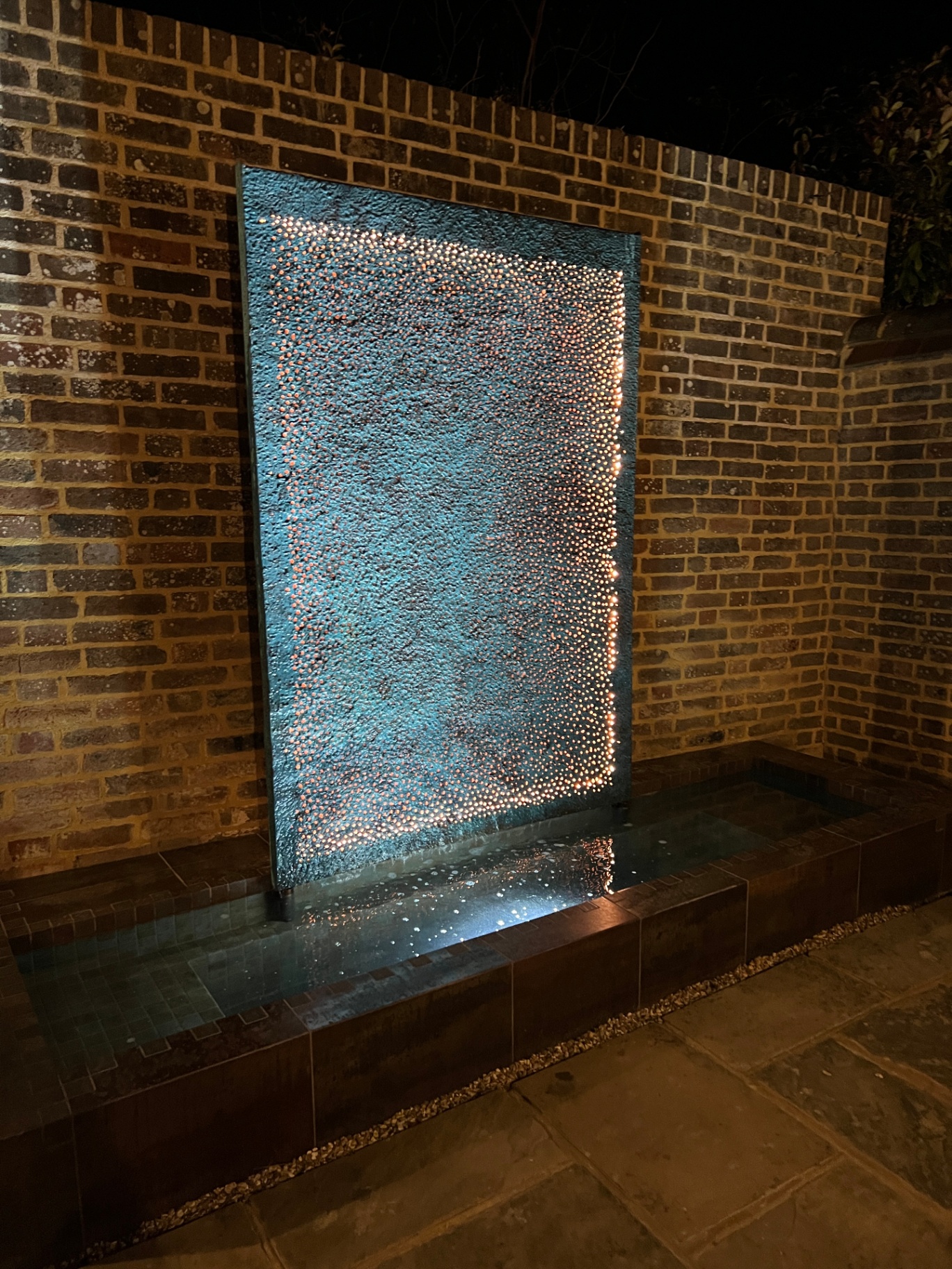 Lava wall lit at night with copper light catching the textured face above the still pool