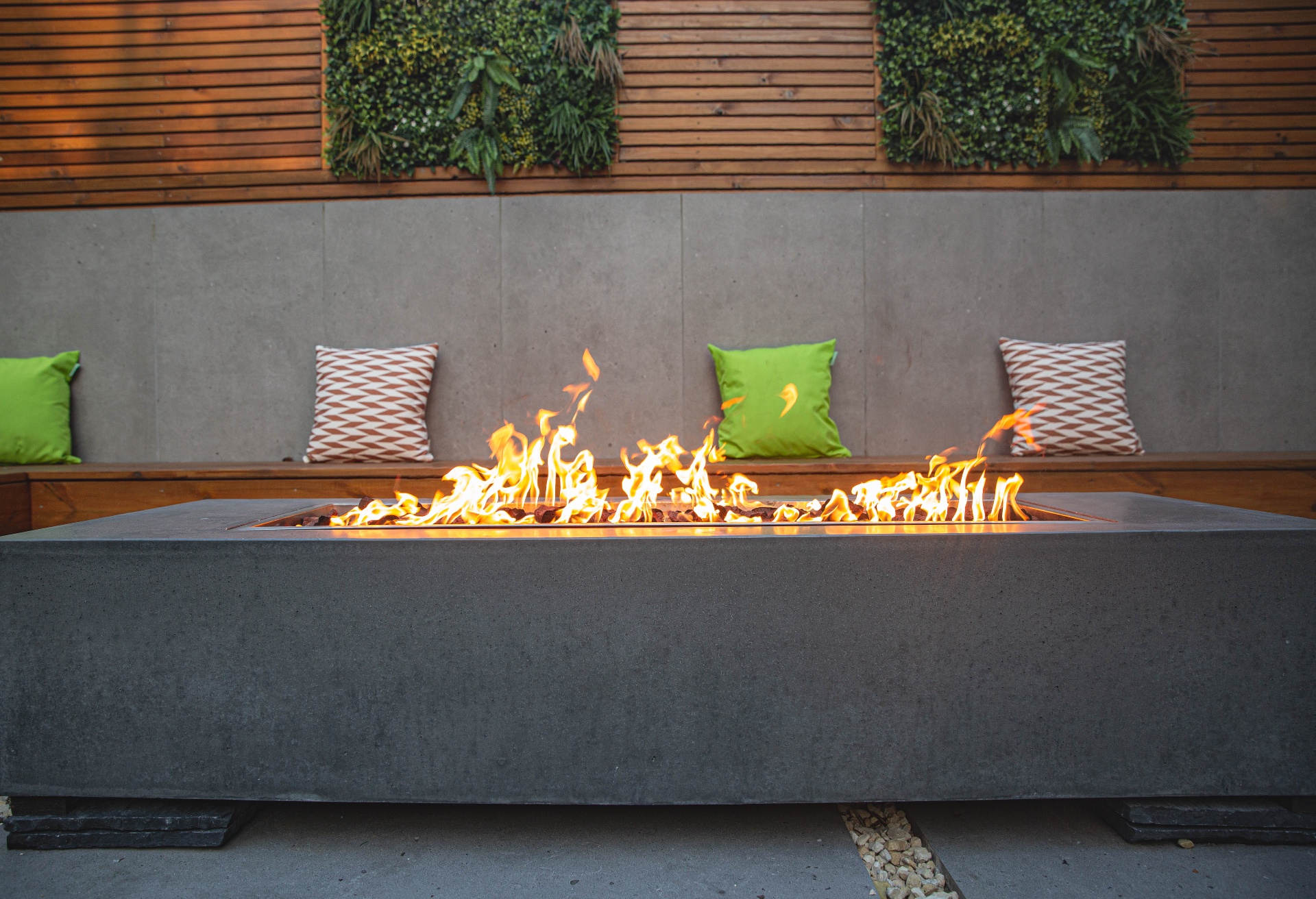Linear concrete fire pit ablaze against cedar slat wall with living green panels