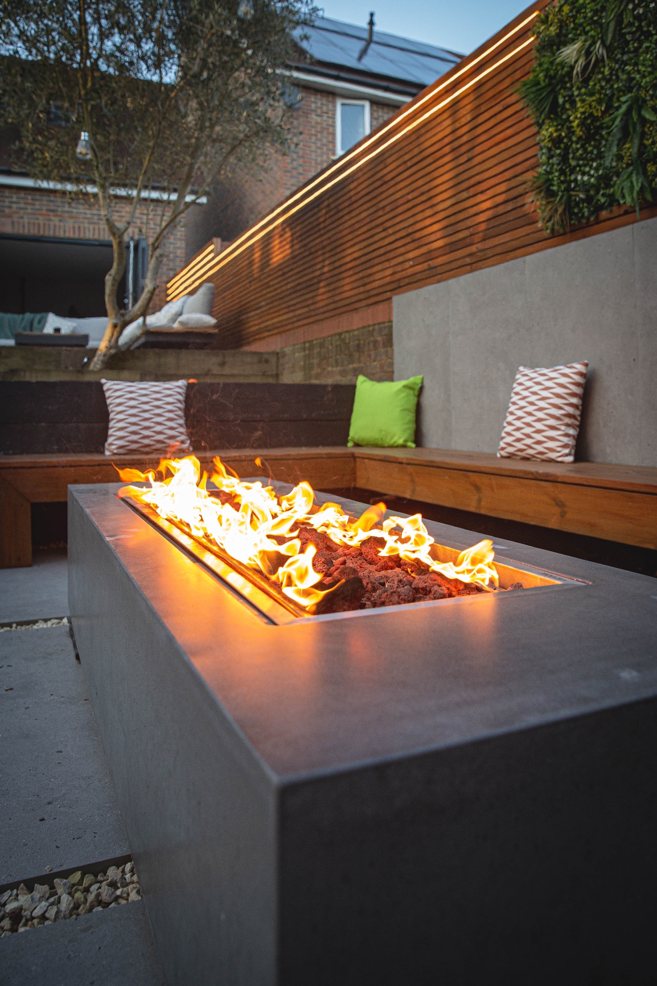 Dusk view of the fire pit flames with warm linear lighting along the cedar screen