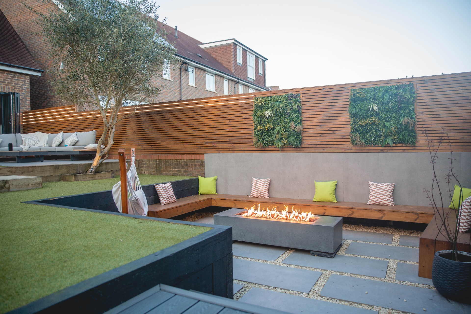 Wide view of the garden with sunken fire pit, bench seating and raised lawn terrace