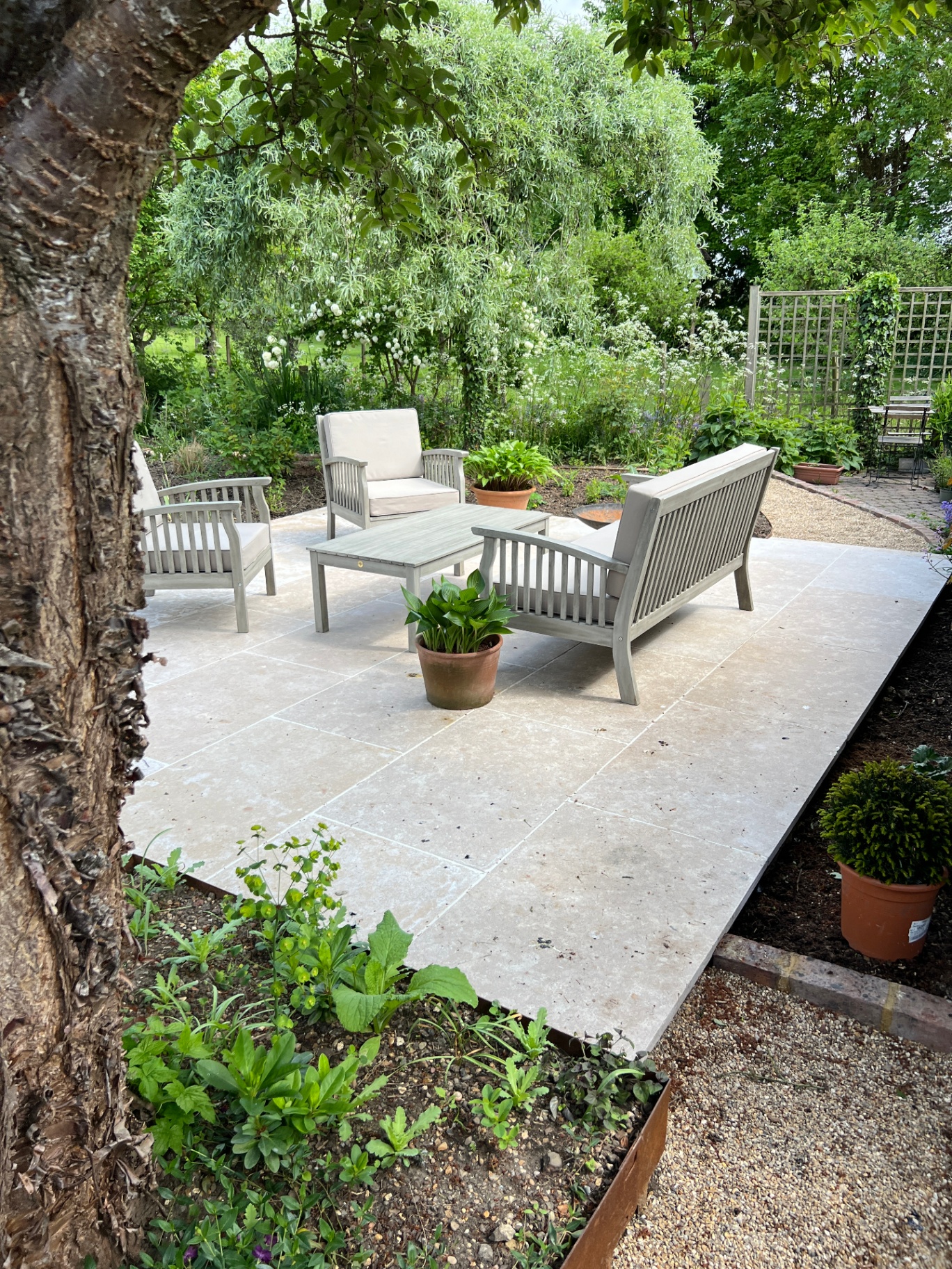 Honed limestone patio with grey teak lounge set framed by willow and lush borders
